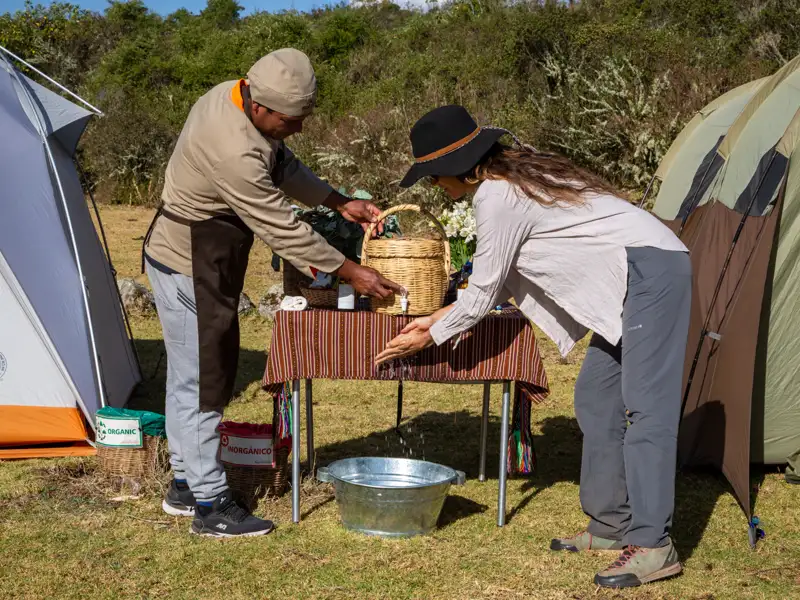 Reisende wäscht sich im Camp die Hände, unterstützt von einem Mitarbeiter.
