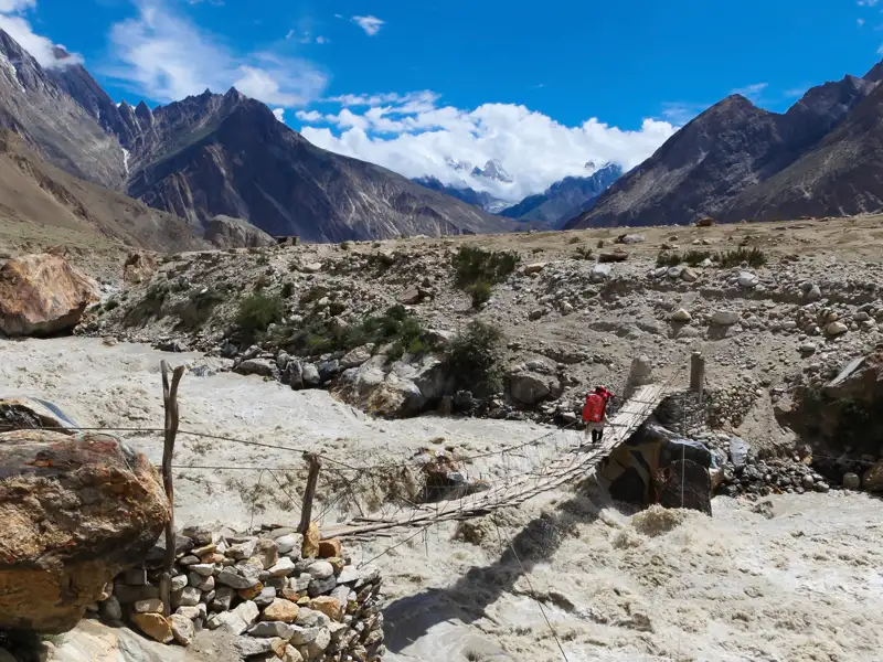 Wanderer überquert eine Hängebrücke über einen reißenden Fluss im Hochgebirge.