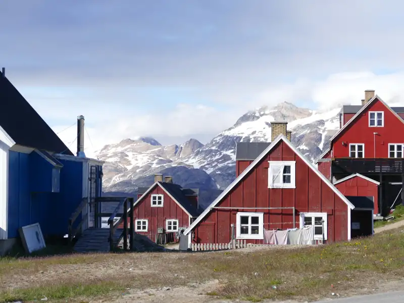 Traditionelle bunte Häuser in einer grönländischen Siedlung vor der Kulisse schneebedeckter Berge.