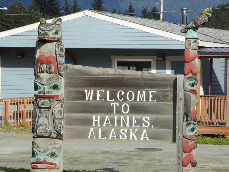 Ein Willkommensschild in Haines, Alaska, mit traditionellen Totempfählen.