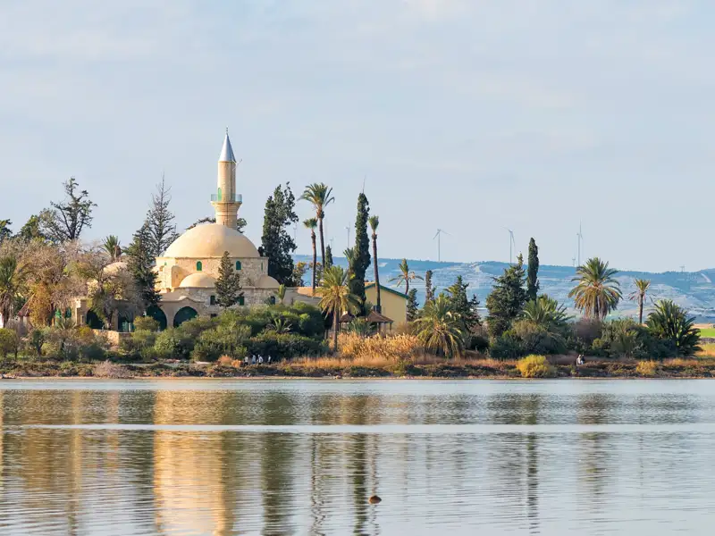 Hala-Sultan-Tekke-Moschee mit dem Salzsee im Vordergrund und Windkraftanlagen in der Ferne.