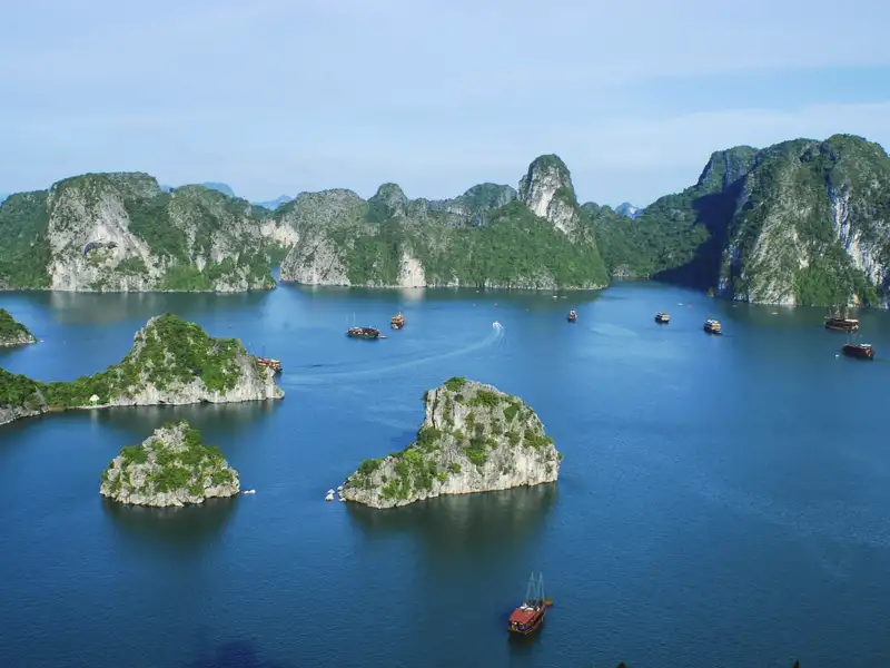 Panoramablick auf die Kalksteininseln und das ruhige Wasser der Halong-Bucht mit traditionellen Dschunken.
