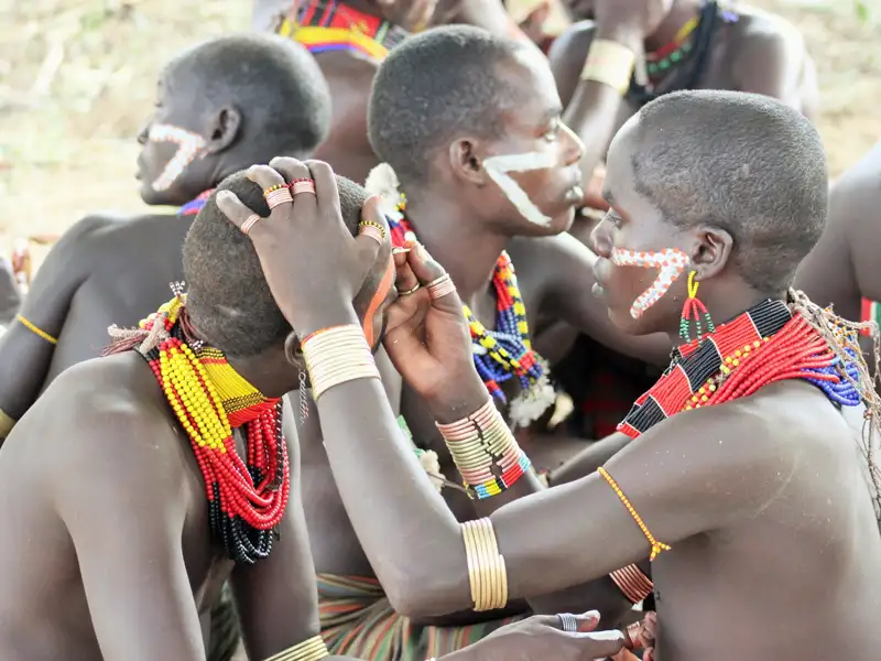 Stammesmitglieder mit traditionellem Schmuck führen eine Gesichtsbemalung durch.