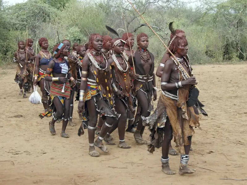 Menschen in traditioneller Kleidung und Schmuck gehen über einen Platz.