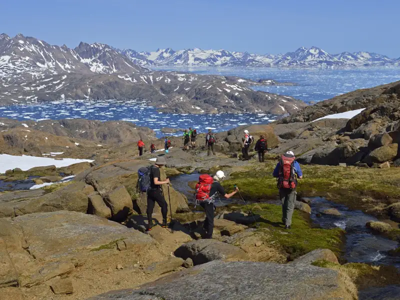 Wandergruppe auf einem Pfad in Grönland, mit Blick auf einen eisbedeckten Fjord im Hintergrund.