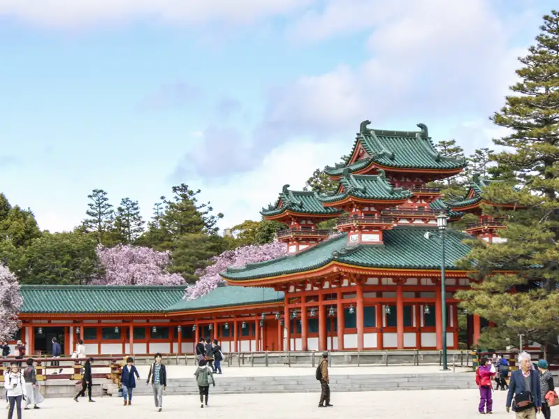 Traditionelle japanische Architektur mit grünen Ziegeldächern und Kirschblüten im Hintergrund.