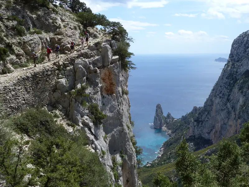 Wanderer auf einem schmalen Küstenpfad mit Blick auf das Meer und Felsformationen.