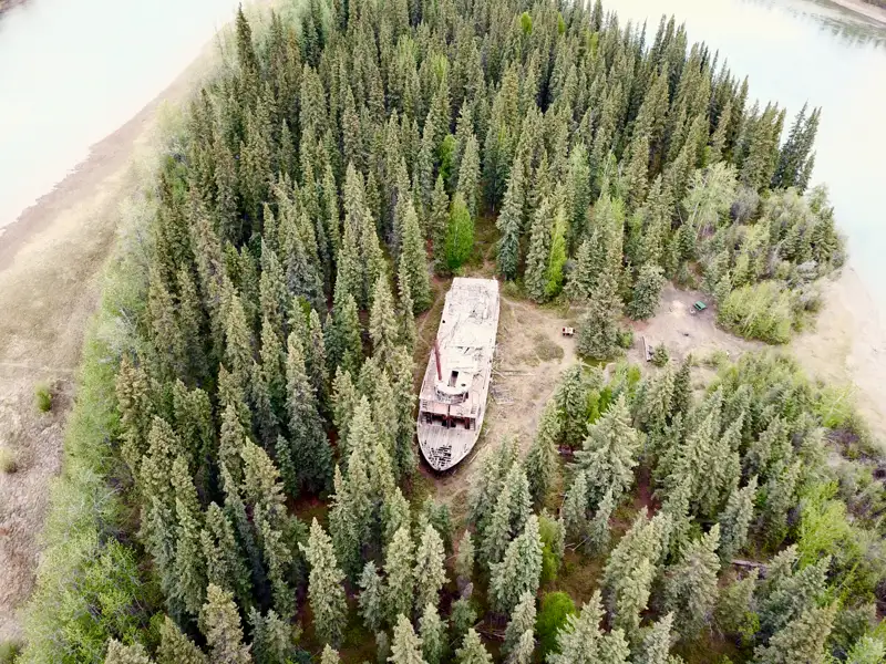 Luftaufnahme eines verlassenen Schiffswracks, das von Bäumen umgeben ist.