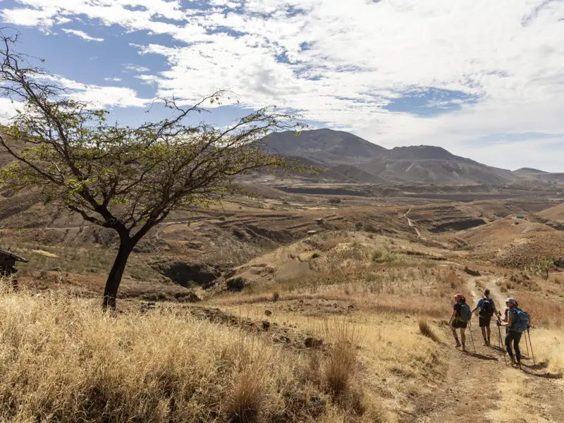 Wandergruppe auf einem Pfad in einer trockenen, vulkanischen Landschaft.