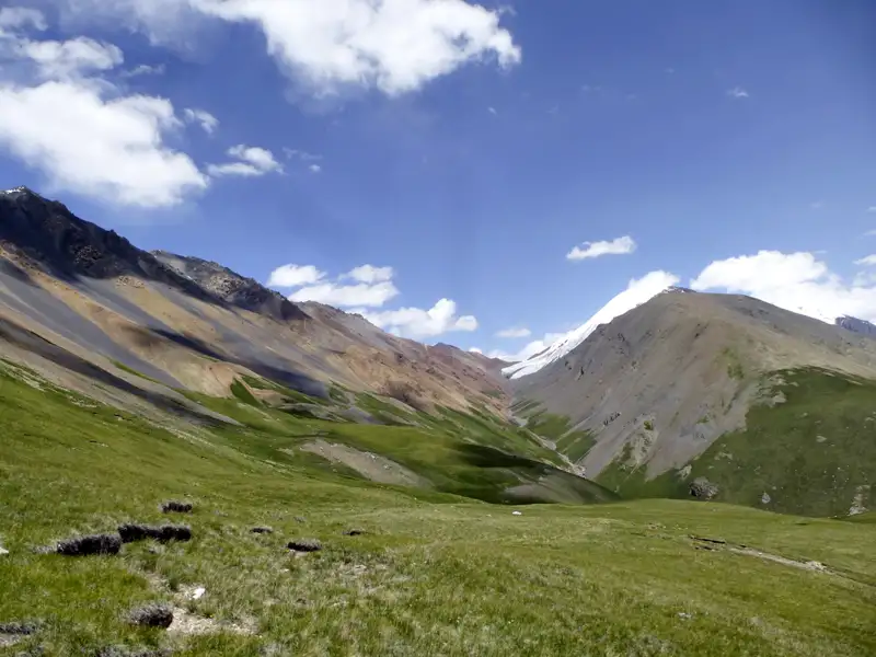 Grüne Hügellandschaft und Gebirge mit bunten Gesteinsschichten.