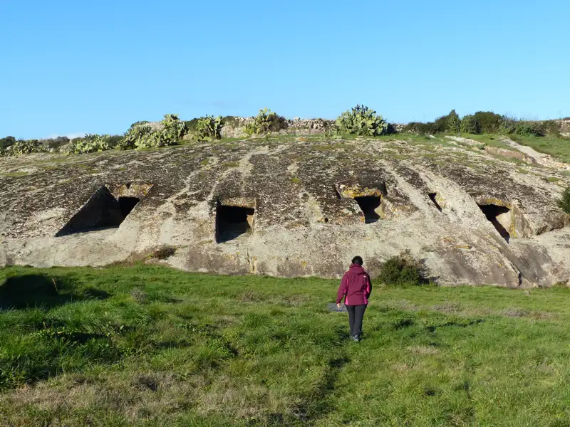 Felsengräber mit rechteckigen Eingängen in einer Hügellandschaft.