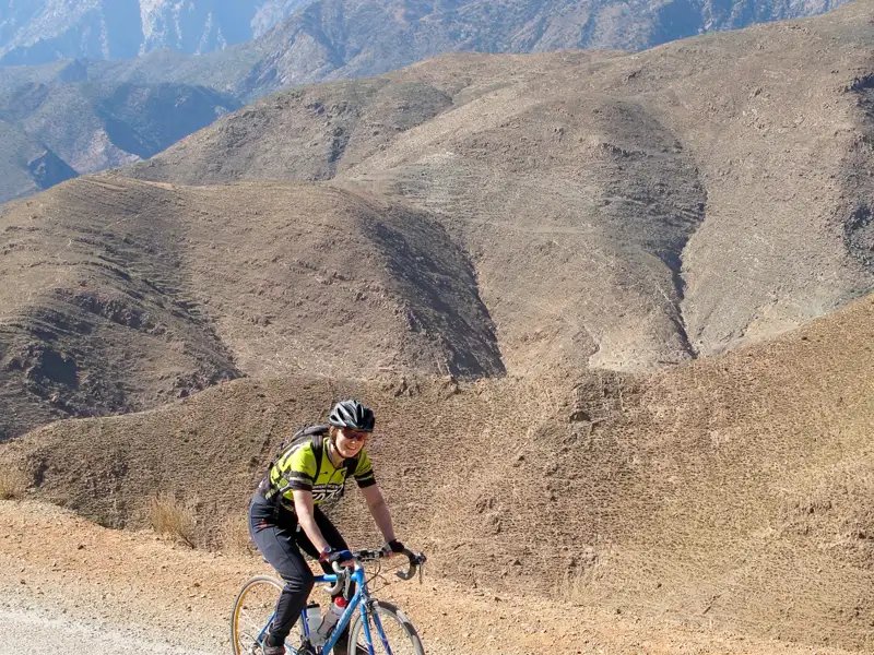 Radfahrer auf Bergstraße mit hügeliger Landschaft im Hintergrund.