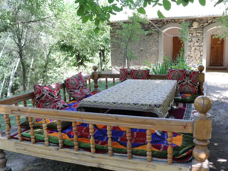 Traditioneller Essbereich im Freien mit Holztisch, -bänken und bunten Textilien.