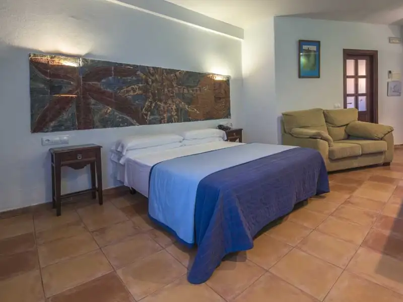 Doppelbett im Hotelzimmer mit blauer Decke und beigefarbenem Sofa.