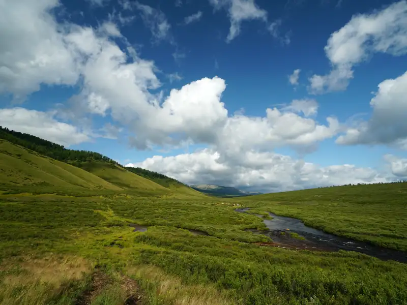 Grüne Hügellandschaft mit einem Fluss unter einem bewölkten Himmel.