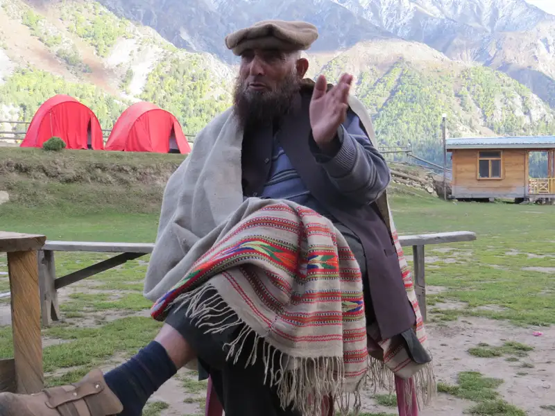 Ein lokaler Mann in traditioneller Kleidung sitzt vor dem Campingplatz in den Bergen.