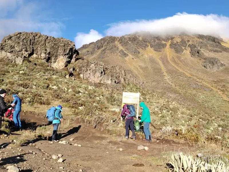 Wanderer machen eine Pause an einem Schild auf einem Bergwanderweg.