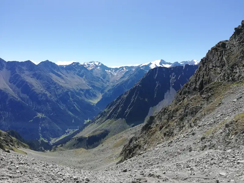 Panoramablick auf ein alpines Tal mit schneebedeckten Berggipfeln.