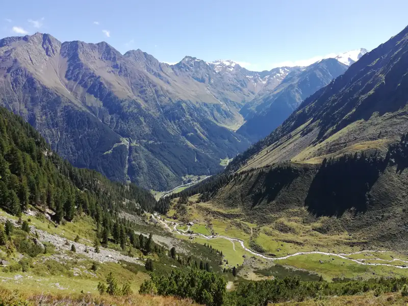 Blick auf ein Alpental mit Fluss und schneebedeckten Bergen.