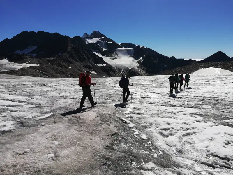 Wandergruppe mit Rucksäcken und Wanderstöcken überquert einen Gletscher in den Bergen.