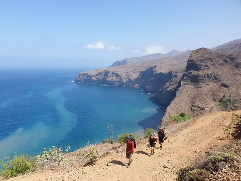 Wanderer auf einem Küstenpfad mit Blick auf das Meer und die felsige Küste.