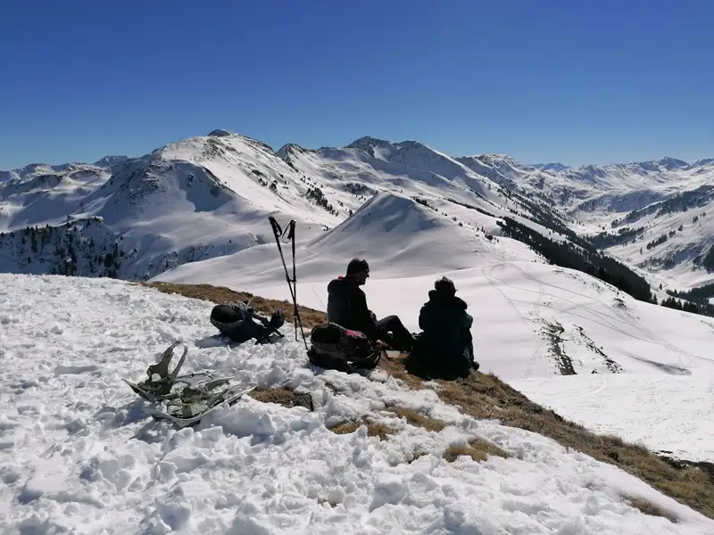 Schneeschuhe und Wanderstöcke liegen im Schnee, während Wanderer eine Pause in den Bergen einlegen und die Aussicht genießen.