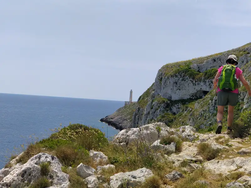 Wanderer auf einem Küstenpfad mit Blick auf einen Leuchtturm.