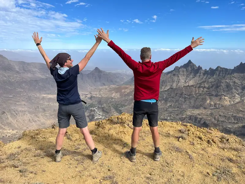 Zwei Wanderer feiern das Erreichen des Gipfels mit erhobenen Armen.