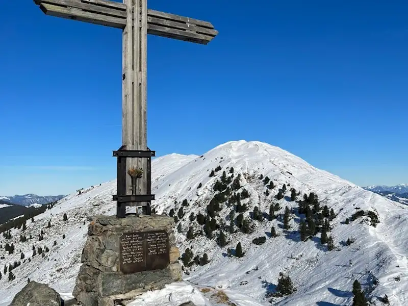 Gipfelkreuz mit Blick auf einen verschneiten Berg.