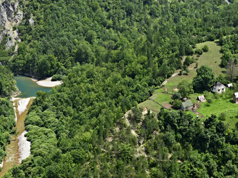 Luftaufnahme eines Flusses und einer ländlichen Siedlung, umgeben von üppiger Vegetation und bewaldeten Hügeln.