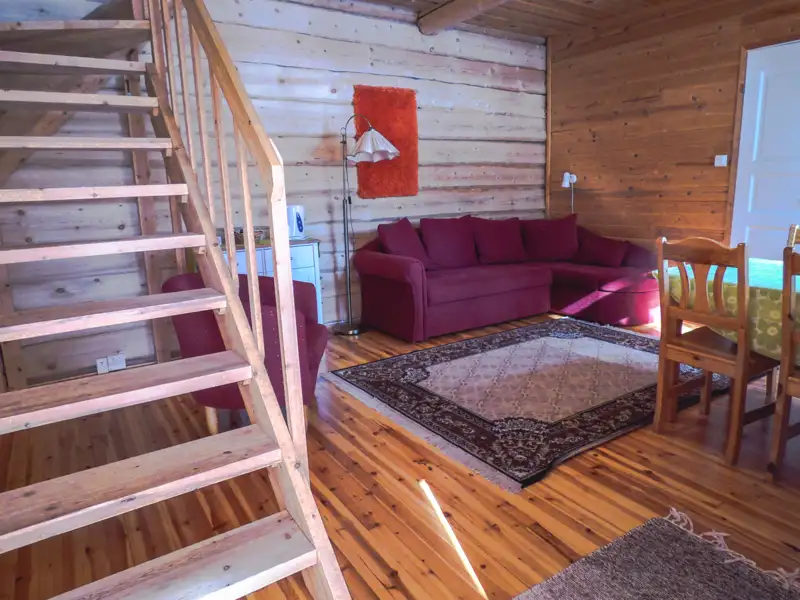 Innenansicht des Wohnbereichs mit Holztreppe, Sofa und Essbereich.