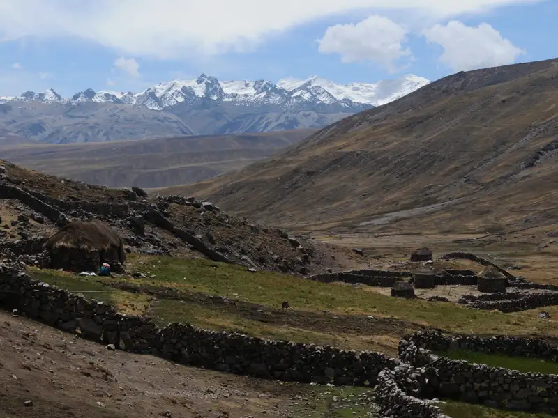 Traditionelle Behausungen und Steinmauern in einem Andental, mit Blick auf die schneebedeckten Berge.