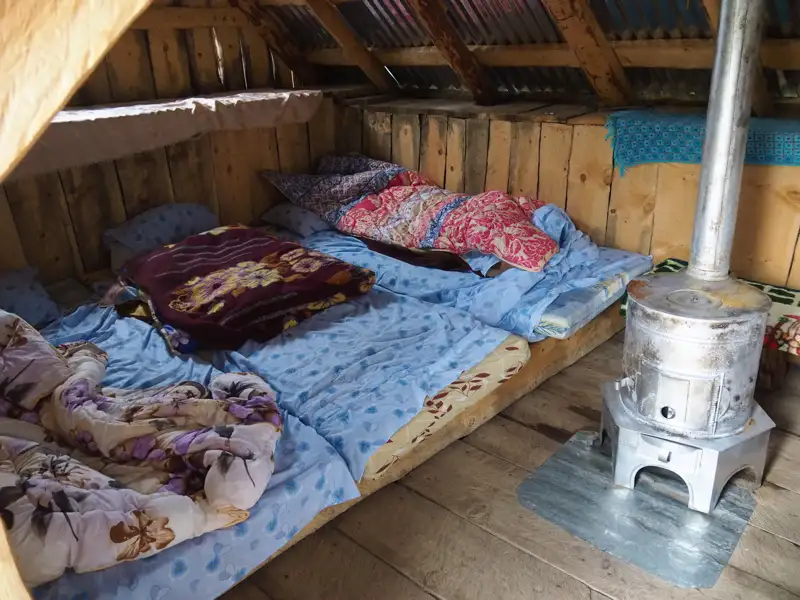 Schlafbereich in einer einfachen Hütte mit Ofenheizung.