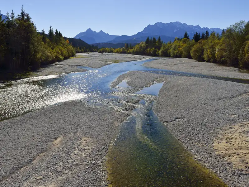 Fluss mit kiesigem Flussbett und Bergen im Hintergrund.