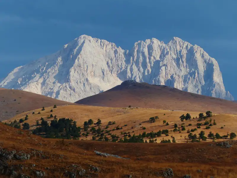 Schneebedeckte Gipfel und herbstliches Hügelland.