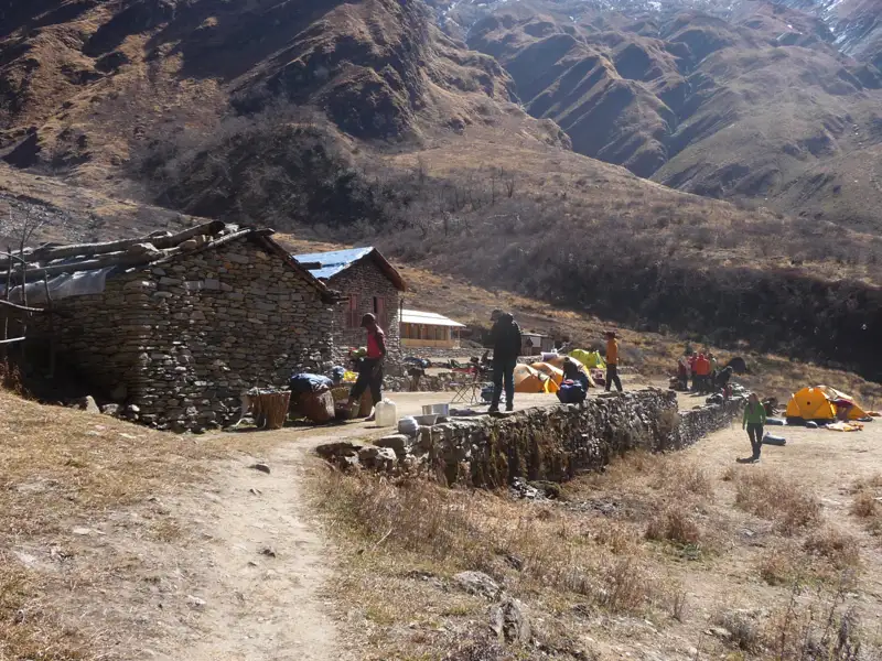 Basislager in den Bergen mit Steinhaus und Zelten, Wanderer bereiten sich auf ihre Tour vor.