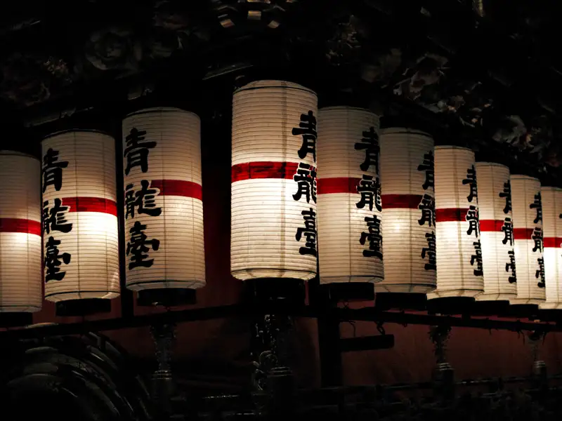 Reihe von beleuchteten japanischen Laternen mit schwarzen Schriftzeichen und roten Streifen.