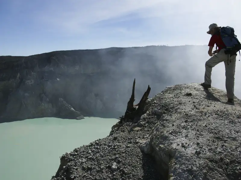 Wanderer am Kraterrand eines Vulkans mit türkisfarbenem See.