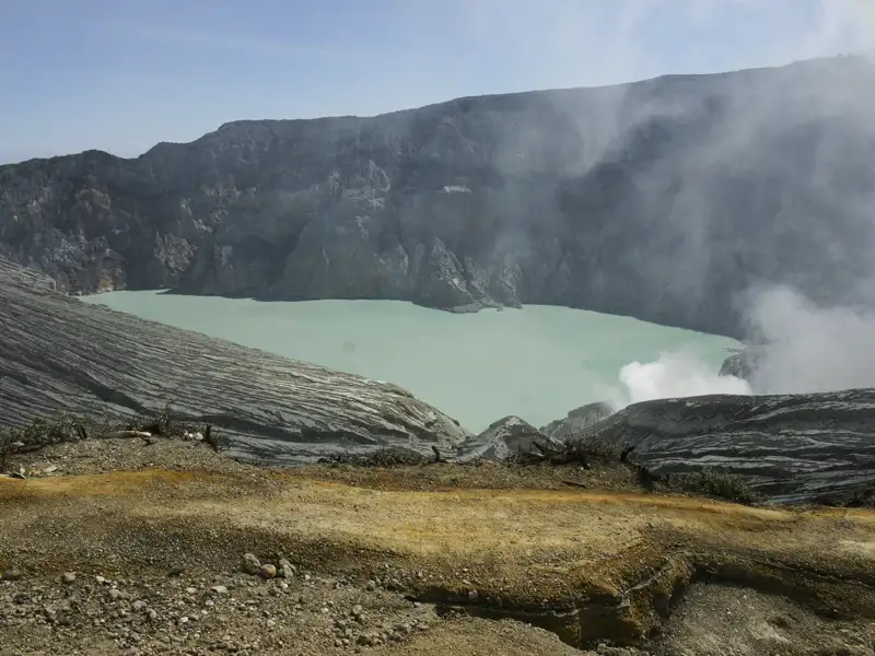 Ausblick auf den Kratersee eines aktiven Vulkans mit sichtbaren Rauchschwaden.