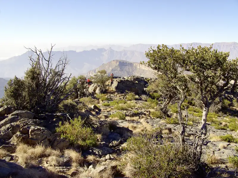 Wanderer erkunden einen felsigen Bergpfad inmitten einer kargen Landschaft mit Blick auf die umliegenden Berge.