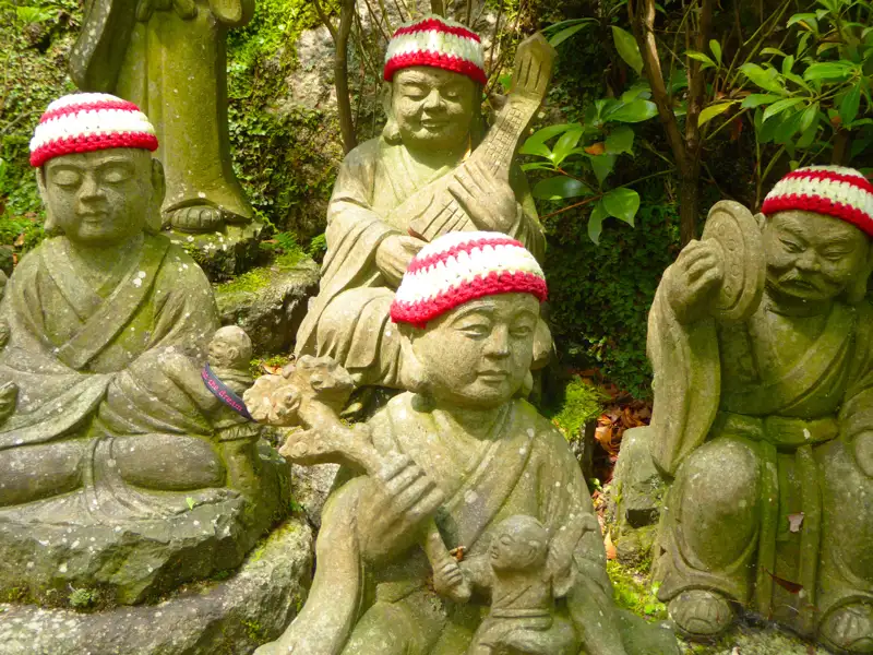 Gruppe von Steinstatuen mit roten und weißen Mützen, möglicherweise religiöse Figuren.