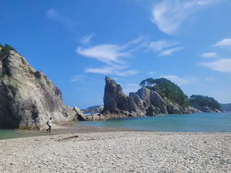 Kiesstrand mit felsigen Klippen und bewachsenen Inseln.