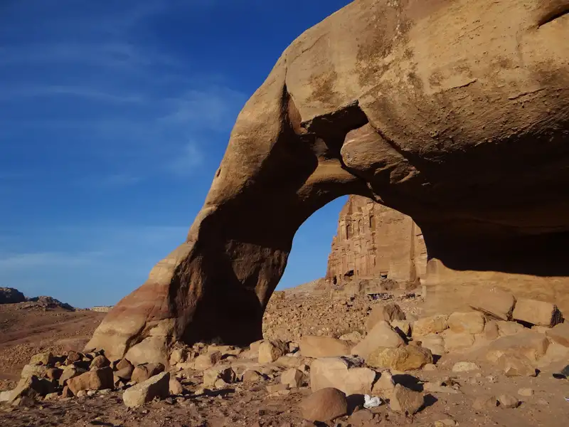 Ein natürlicher Felsbogen in der Wüste rahmt den Blick auf eine historische Stätte ein.