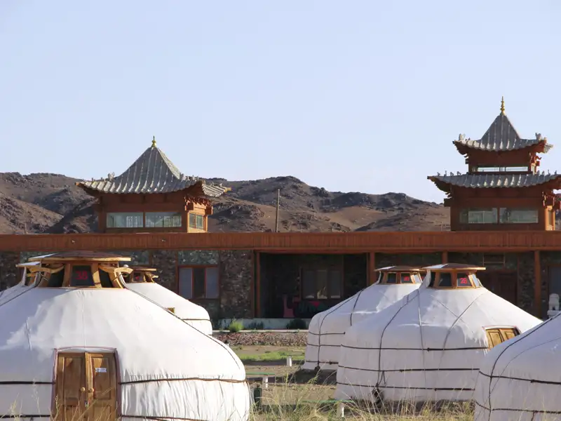Traditionelle Jurten-Unterkünfte vor einem Gebäude mit charakteristischer Architektur.