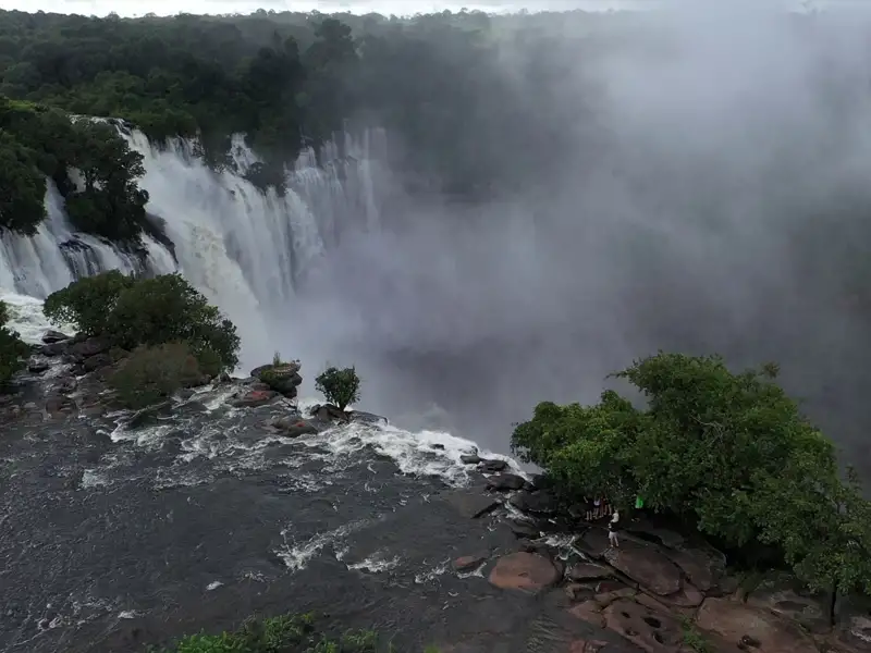 Ein beeindruckender Wasserfall mit starkem Wasserfluss, umgeben von üppiger Vegetation und in Nebel gehüllt.