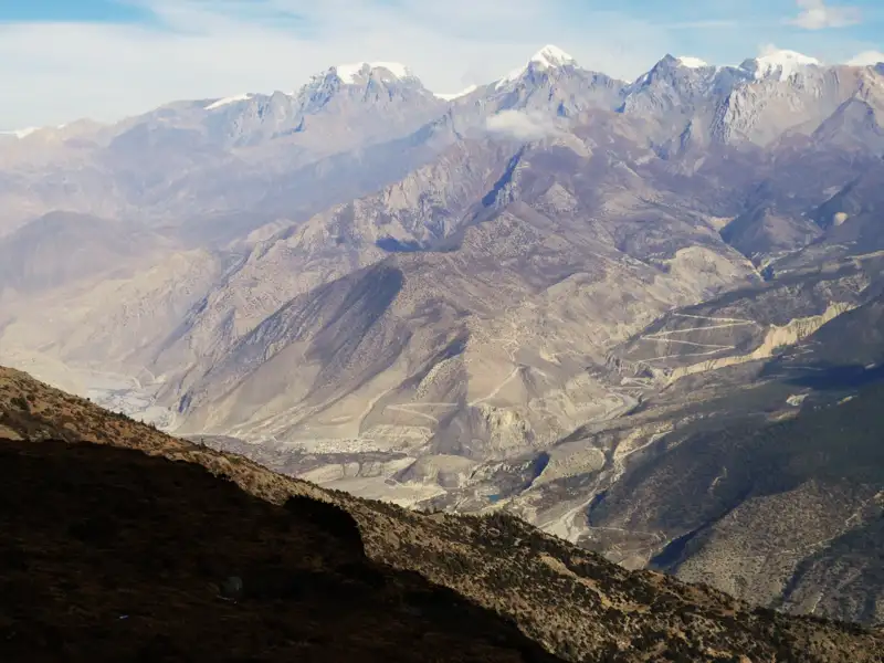Aussicht auf ein Bergtal mit schneebedeckten Gipfeln im Hintergrund.