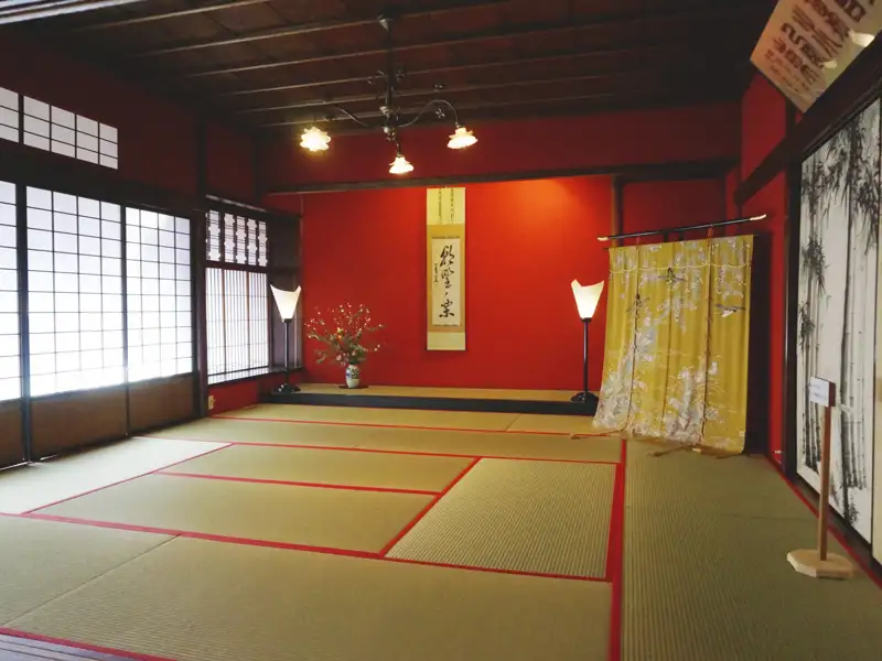 Traditioneller japanischer Raum mit roten Wänden, Tatami-Matten und Schiebetüren.