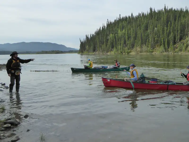 Kanufahren auf einem Fluss mit einem Führer, der vom Ufer aus Anweisungen gibt.