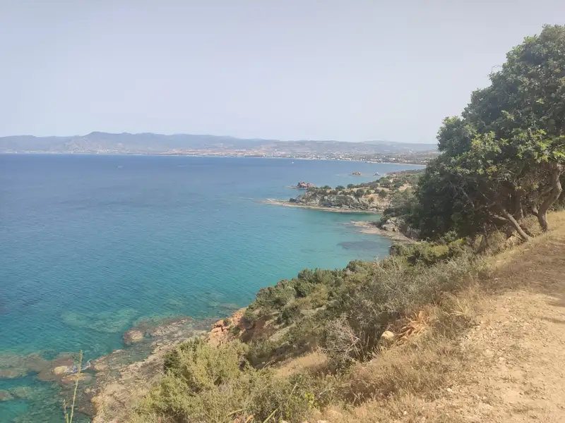 Felsige Küste mit türkisfarbenem Meer und Blick auf die Berge im Hintergrund.