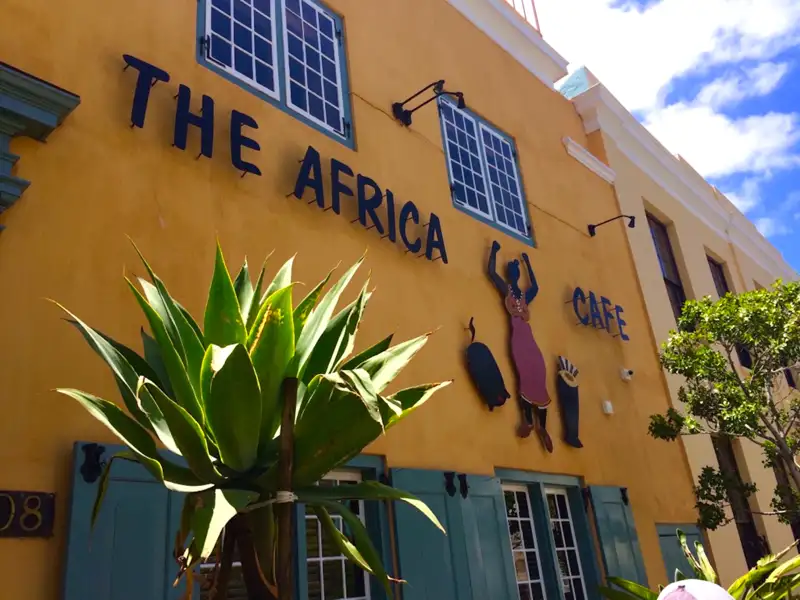 Außenansicht des The Africa Cafe mit gelber Fassade, traditionellen Dekorationen und einer Agave im Vordergrund.